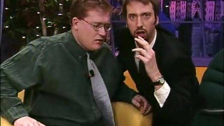 Two men sitting on chairs one making a strange expression