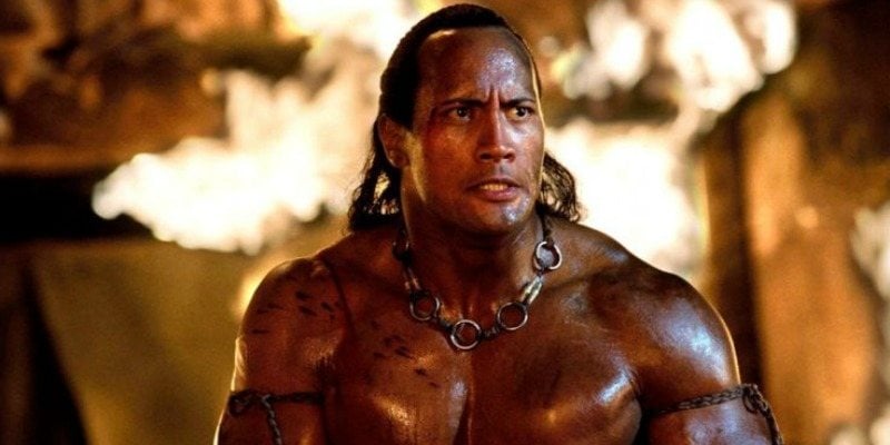 The Scorpion King is shirtless in front of fire.