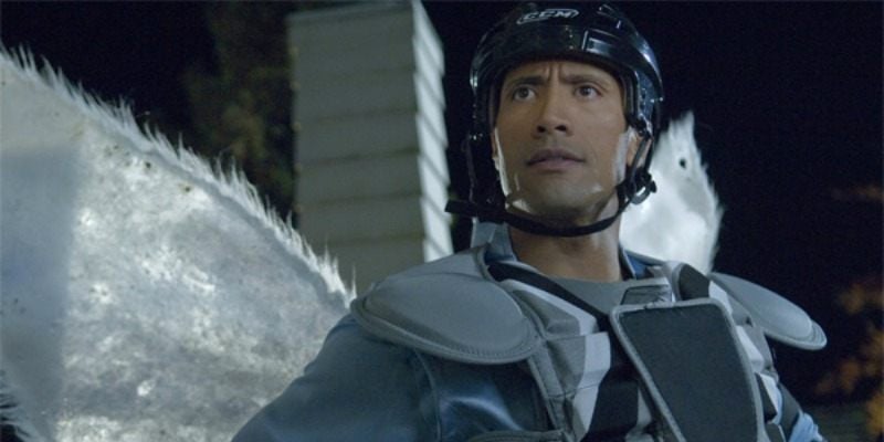 Dwayne Johnson has a chest and shoulder pads on and is wearing wings and a helmet.