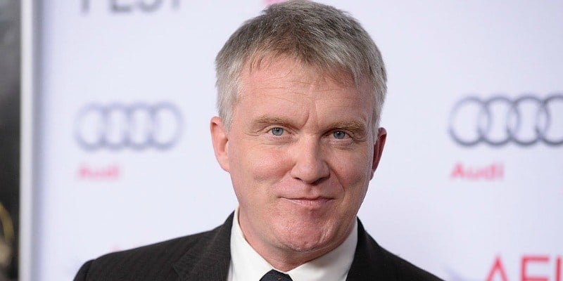 Anthony Michael Hall is smiling in a suit on the red carpet.