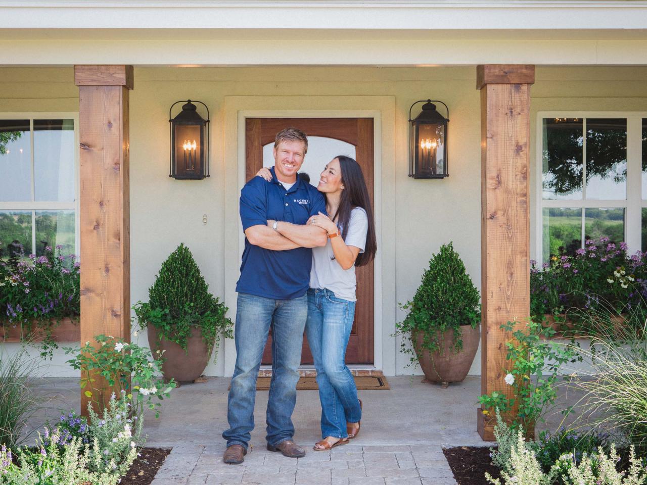 Chip and Joanna stand in front of a house while smiling and laughing. Chip and Joanna stand in front of a house while smiling and laughing.