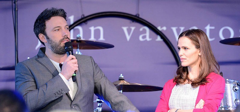Ben Affleck is talking into a microphone on stage as Jennifer Garner is next to him and looking at him.
