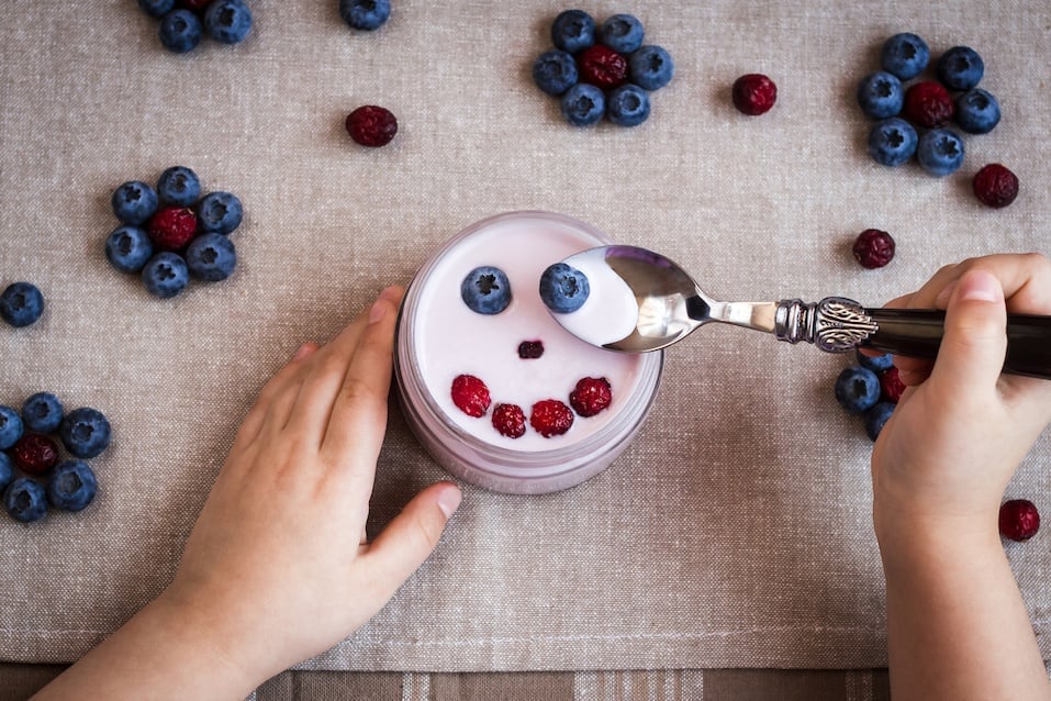 Child hold a spoon with yoghurt and blackberry