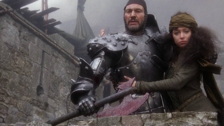 Patrick Stewart in armor holding an axe and Cherie Lunghi holding on to him in Excalibur