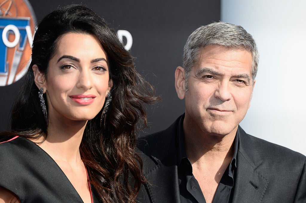 George and Amal Clooney smiling for the camera together on the red carpet.