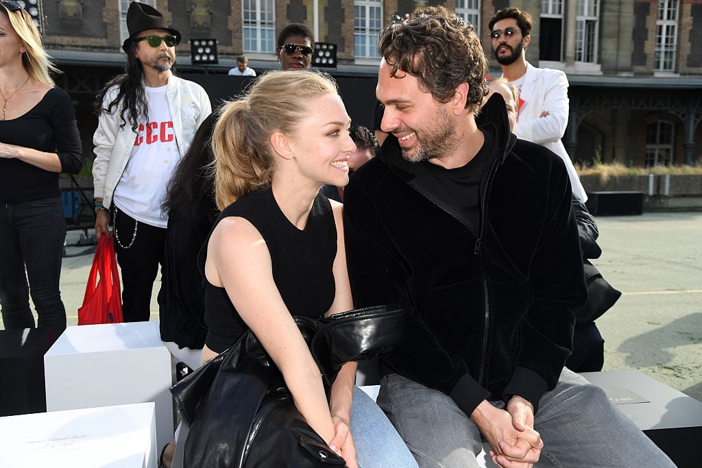 Amanda Seyfried and Thomas Sadoski sitting together at Paris Fashion Week, smiling at each other