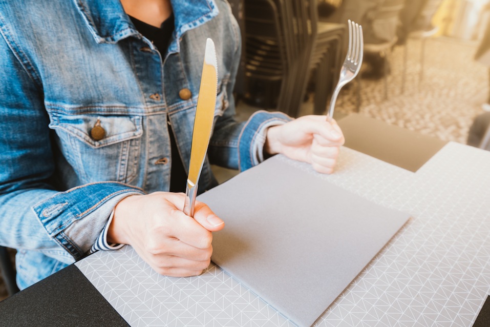 Hungry woman holding knife and fork over empty plate