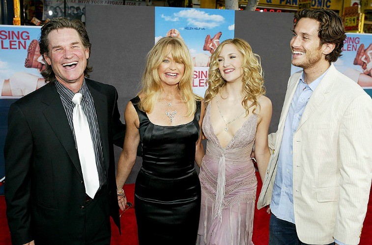 Kurt Russell, Goldie Hawn, Kate Hudson, and Oliver Hudson smiling with their arms around each other on the red carpet