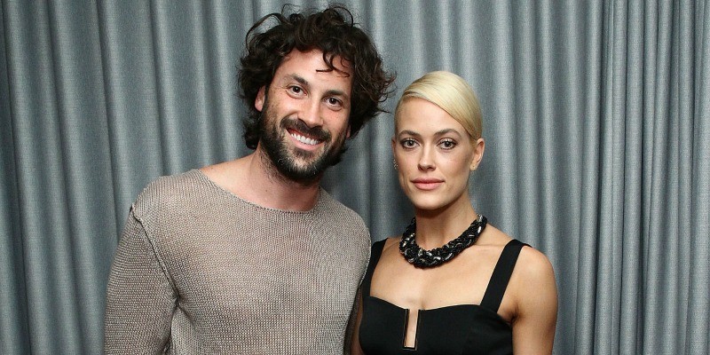 Maksim Chmerkovskiy and Peta Murgatroyd pose together with their arms around each other in front of a grey curtain.