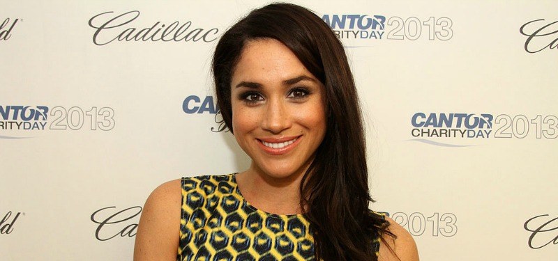 Meghan Markle is smiling in a black and yellow dress on the red carpet.