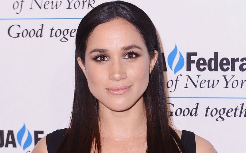 This is a closeup of Meghan Markle wearing a black dress on the red carpet.