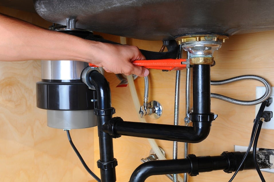 A plumber uses a wrench to tighten a fitting beneath a kitchen sink.
