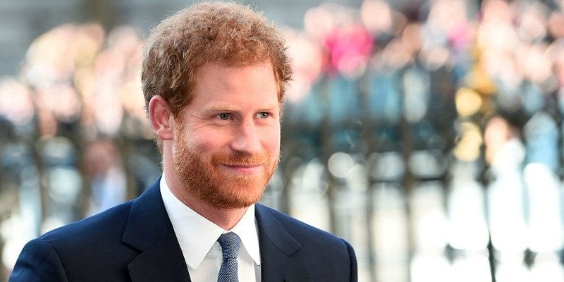 Prince Harry is smiling and in a dark suit.