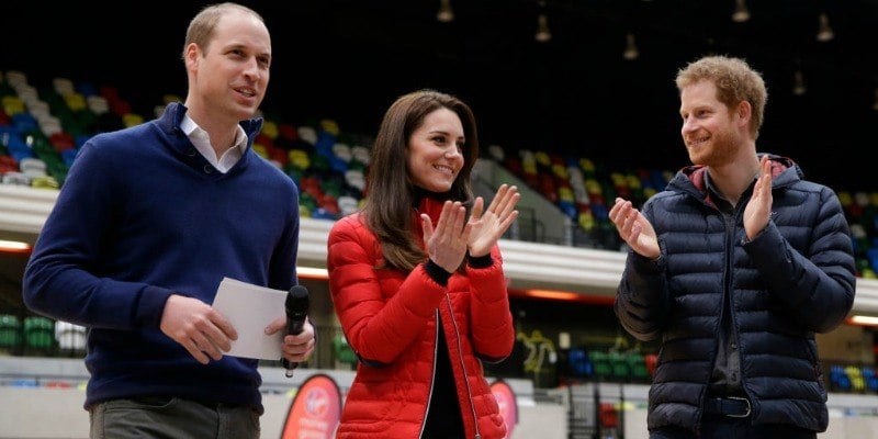 Prince William, Duchess Kate Middleton, and Prince Harry are clapping at a stadium full of people.