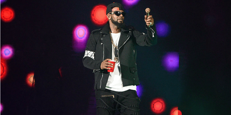 R. Kelly is on stage holding a microphone and red cup. R. Kelly is on stage holding a microphone and red cup.