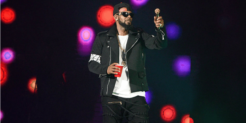 R. Kelly is on stage holding a microphone and red cup.