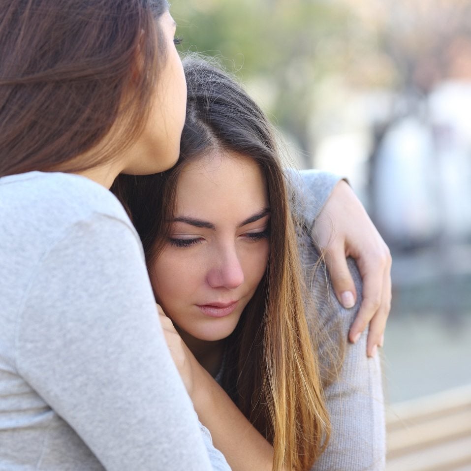 Sad girl crying and a friend comforting her outdoors