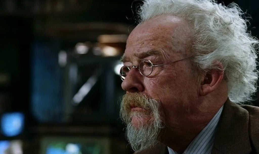 John Hurt with glasses on, looking to the left of the frame