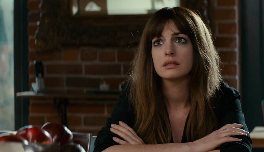 Anne Hathaway sitting at a table with her arms folded
