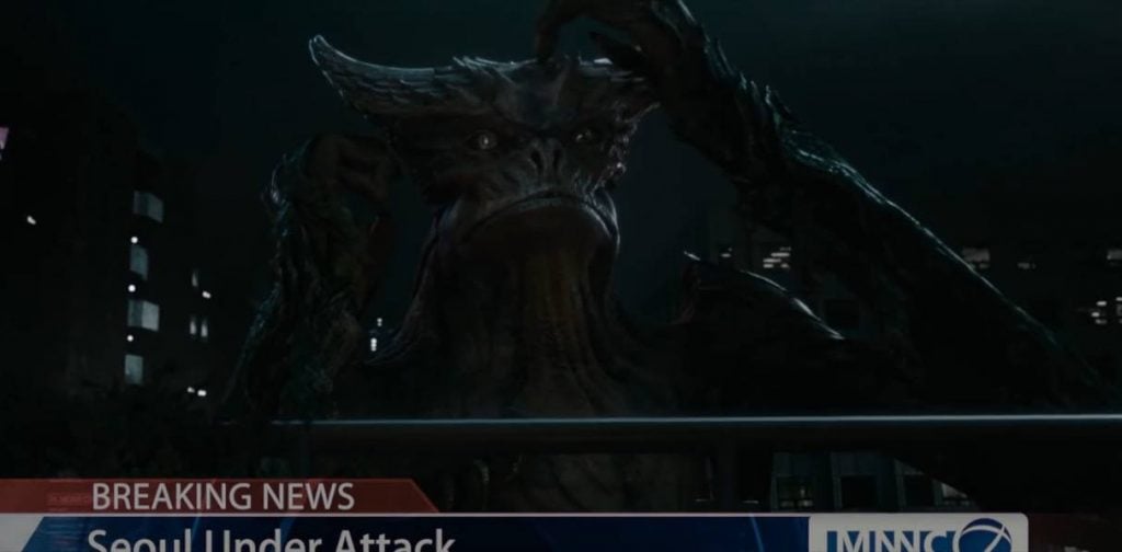 The monster in Colossal scratching its head while on a newscast