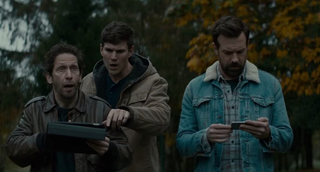 The cast of Colossal in a park, looking down at an iPad screen together