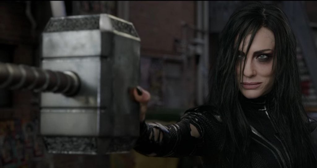Hela holds Thor's hammer out in front, looking to the left of the frame
