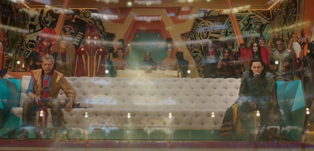 Grandmaster and Loki sitting on either side a long white couch
