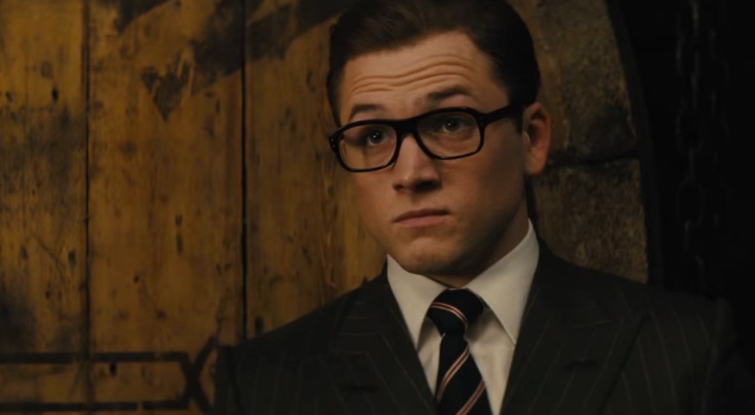 Taron Egerton with his eyebrows raised, wearing a suit