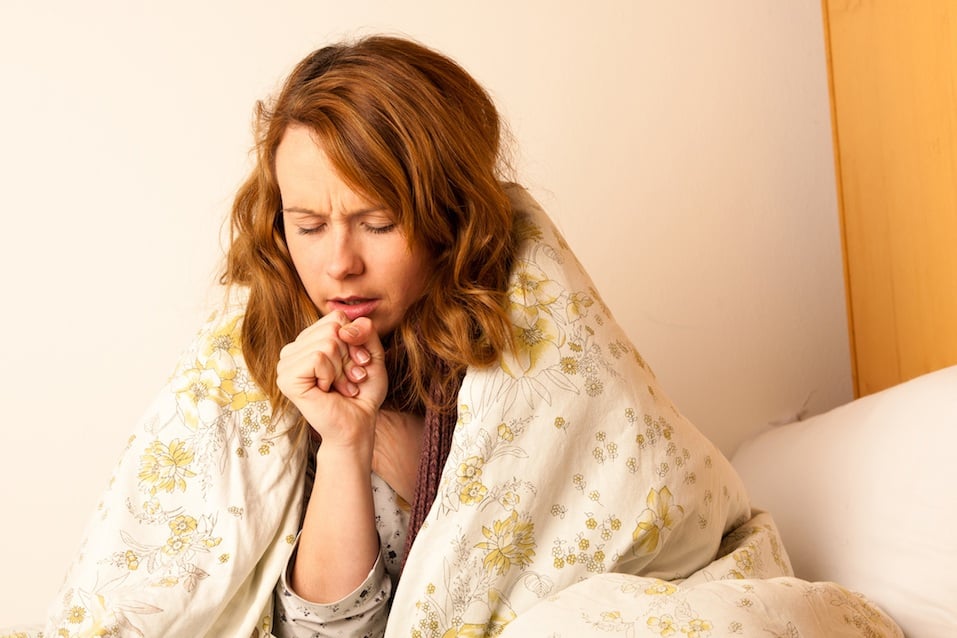 Sick woman coughing in bed under a blanket