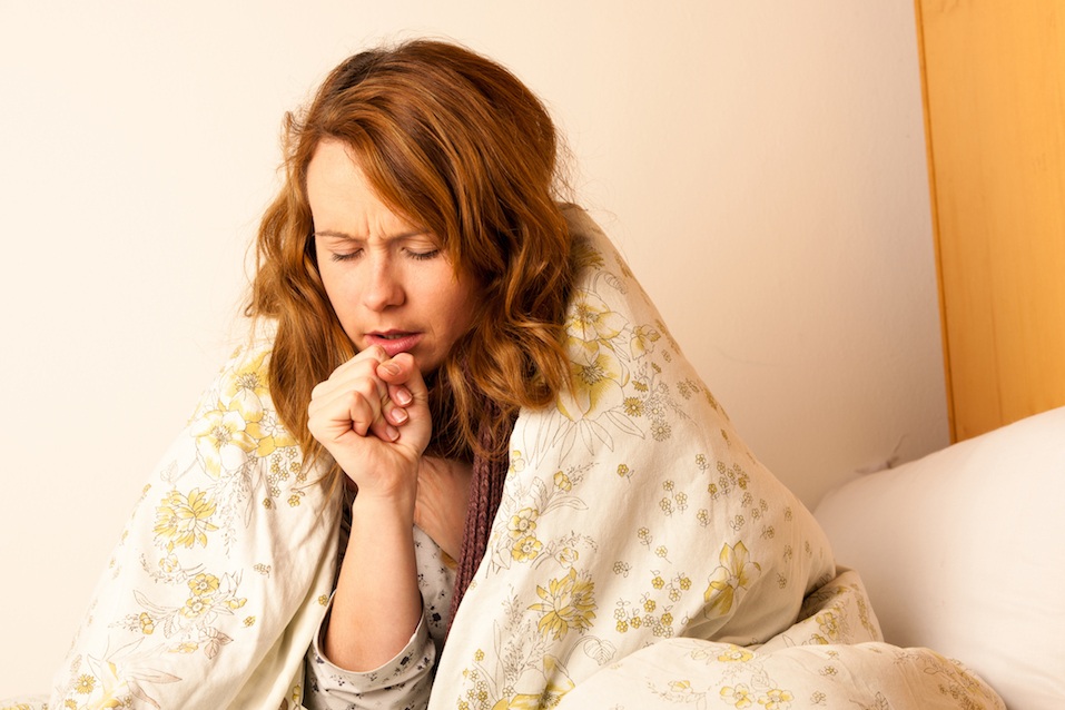 Sick woman coughing in bed under a blanket