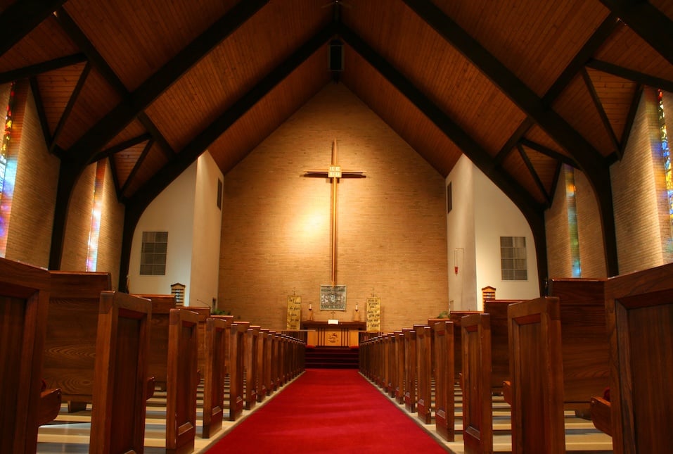Inside of a large, modern church with pews and cross visible.
