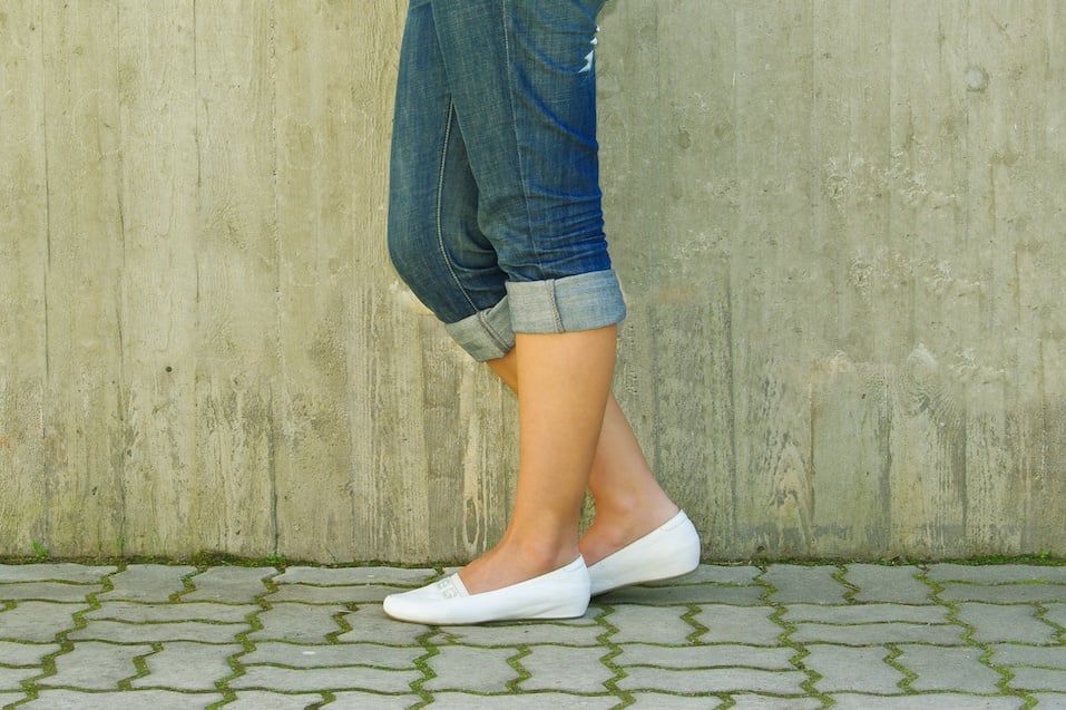 Woman's legs in jeans rolled up wearing white shoes
