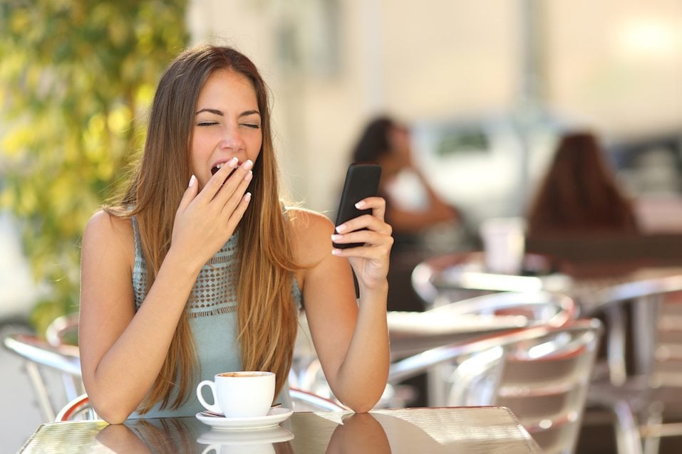 Woman yawning while is working on the phone at breakfast in a restaurant