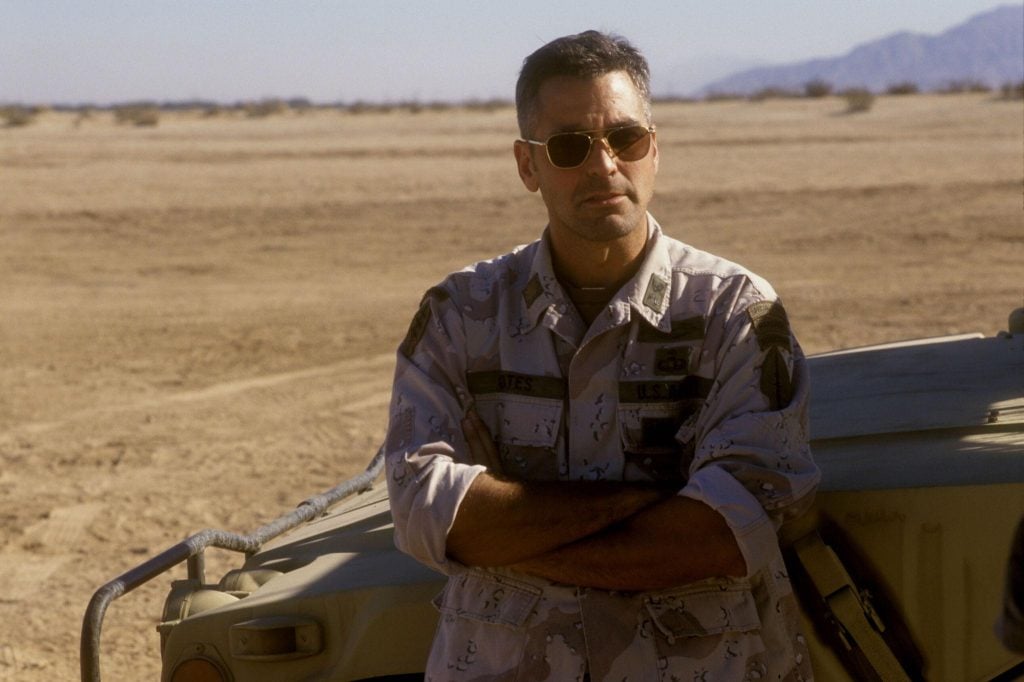 George Clooney wearing army fatigues, leaning against a jeep