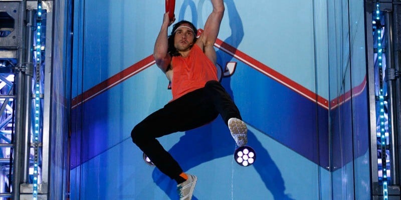 Jake Murray in a red tank top swinging from ring to ring while competing