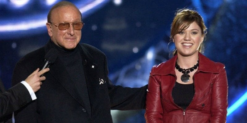 Clive Davis and Kelly Clarkson are standing next to each other on stage of American Idol.