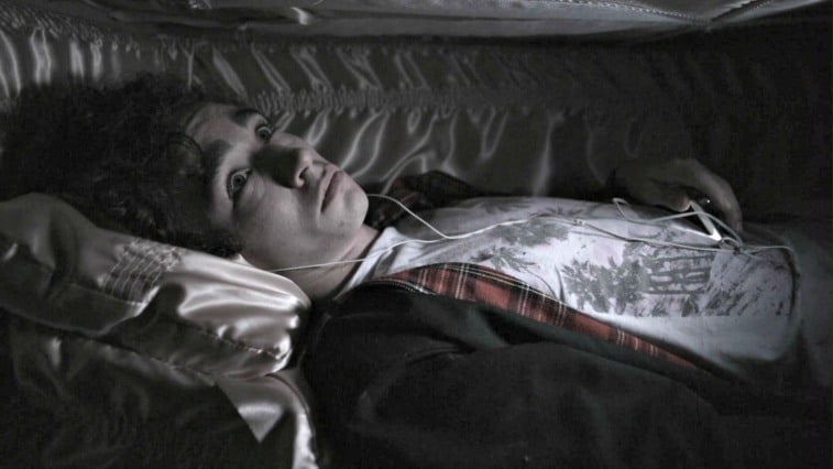 Robert Sheehan as Nathan Young with headphones in listening to an MP3 player in a coffin on Misfits 
