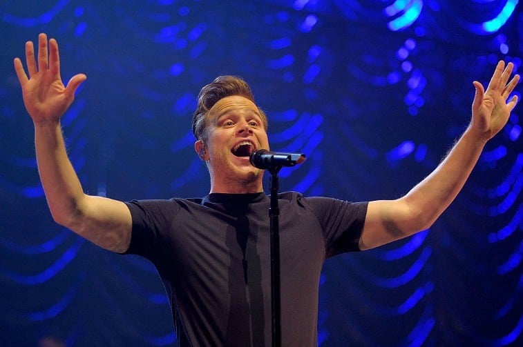 Man on stage singing into a microphone with his arms in the air