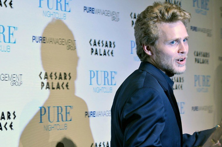 Man posing for paparazzi in front of backdrop advertising Pure Nightclub and Caesars Palace