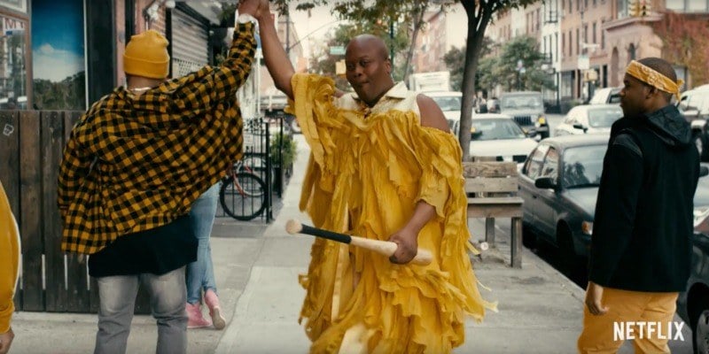 Tituss is dressed up as Beyonce and a bat in one hand and is high fiving someone else with the other.