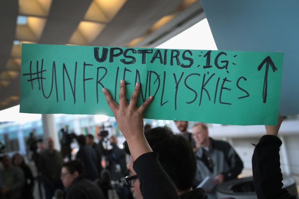 a protester holds an "unfriendly skies" sign at a protest united airlines protest