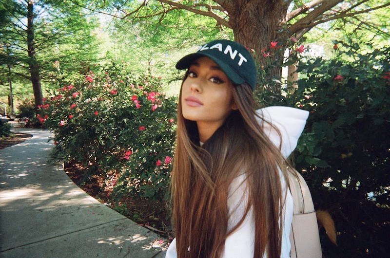 Ariana Grande poses in a baseball cap in front of flowers