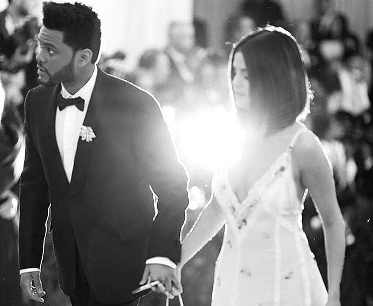 A black-and-white photo of Selena Gomez and The Weeknd walk up the stairs at the 2017 Met Gala