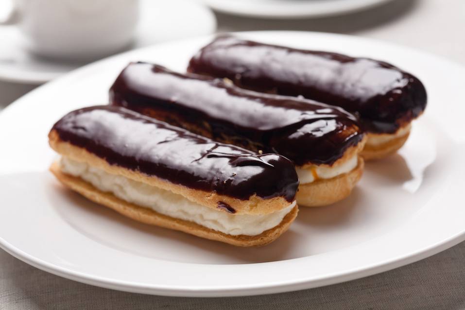 three chocolate cream eclairs on a white plate
