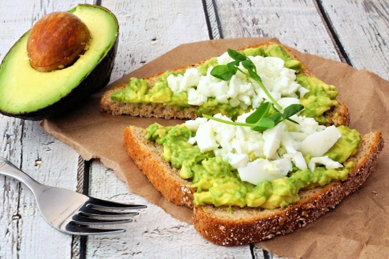 Avocado toast with egg whites and pea shoots on paper against a white wood background