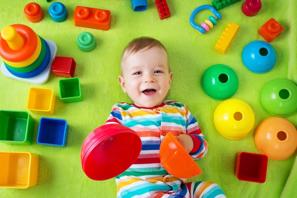 Baby liegt auf der Decke mit vielen Spielsachen herum