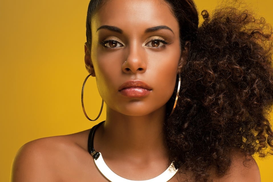 Beautiful African-American woman wearing golden jewelry and posing in front of a yellow background