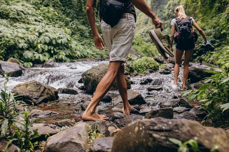 man and woman crossing the stream barefooted