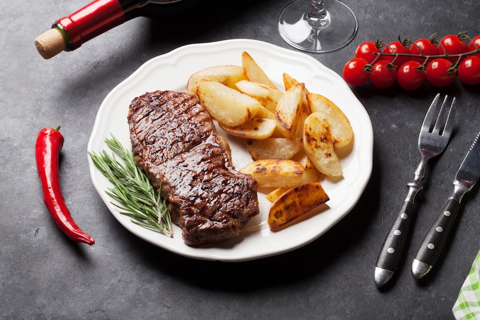 Grilled striploin steak with potato and red wine over stone table