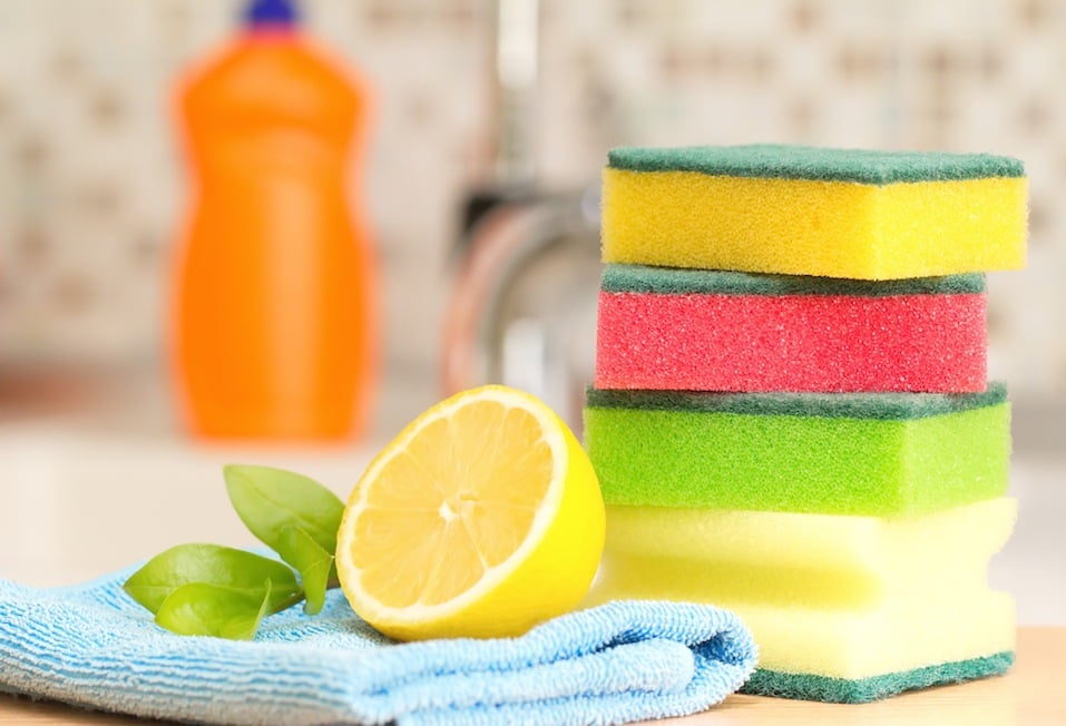 stack of sponges next to a lemon by a kitchen sink and dishwasher